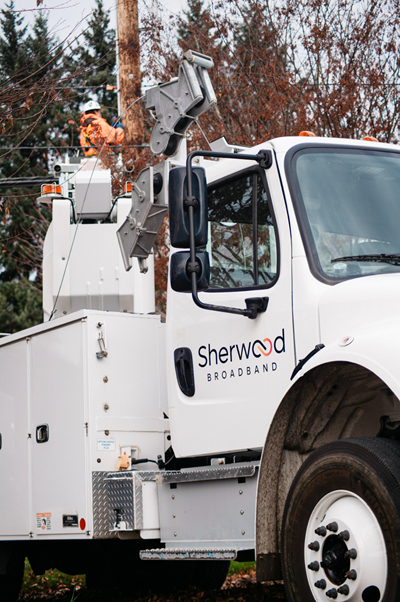 Sherwood Broadband utility truck with worker climbing utility pole in background