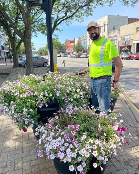 City worker in yellow reflector shirt waters a pot of flowers along street in Downtown Wadsworth Ohio