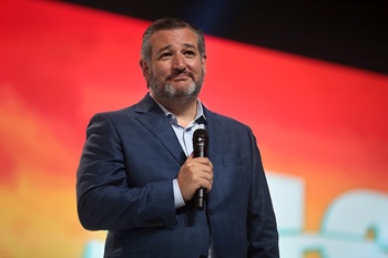 Sen. Ted Cruz stands on stage holding a mircophone smirking