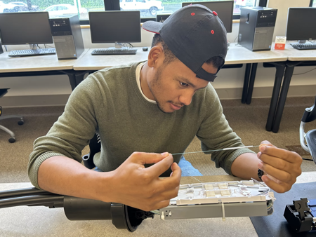 A teenager in a computer class stares at fiber strand about fiber splice case