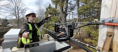 A teenager wearing a hard hat working on fiber splice case on utility pole