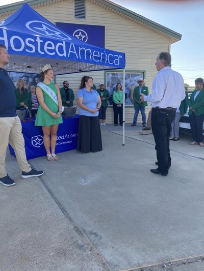 Monahans TX Hosted American Event A beauty pageant contestant stands outside Hosted America tent covered table speaking to community member