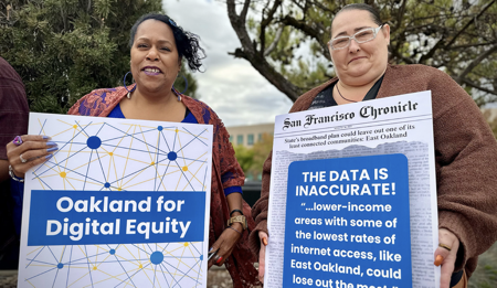 Two women in Oakland hold up signs calling for digital equity