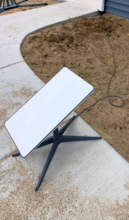 Starlink dish on ground A Starlink dish, which is shaped like a square, sits on a walkway to a home