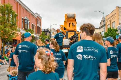 A group of Traverse City utility workers wearing work t shirts walk down downtown Traverse City street in a city parade