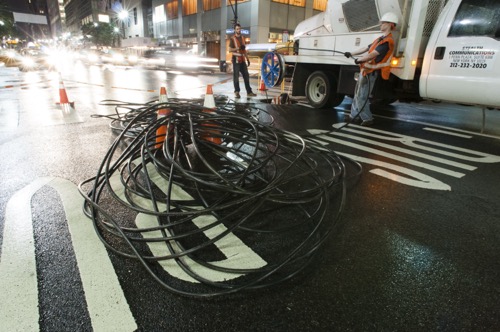A crew pulls fiber at a Manhattan intersection at night