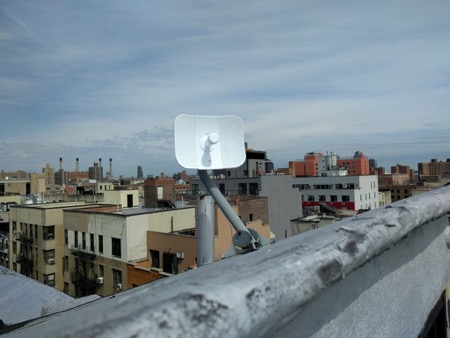 NYC Mesh receiver affixed to side of building overlooking other buildings in NYC 