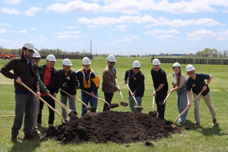 A dozen city officials holding shovels above a mound of dirt at groundbreaking ceremony