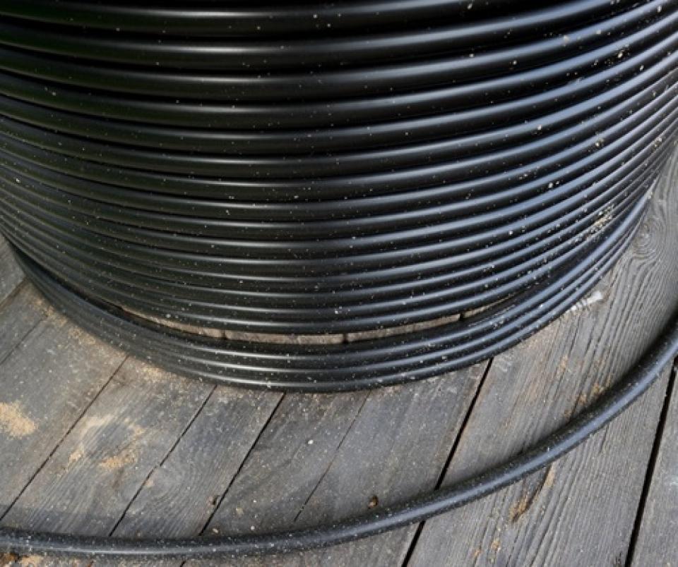 A spool of black encased fiber sits on top of wooden floorboard