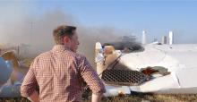 Elon Musk stands with his hands on his hip, back to camera surveying exploded rocket debris