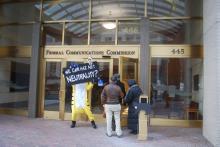 A protestor wearing a cat suit holds a sign in favor of Net Neutrality in front of entrance to FCC building