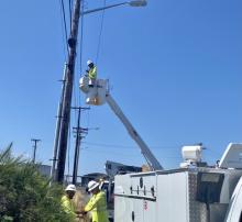 A utility crew member is aloft in a bucket truck installing aerial fiber lines on a utility pole