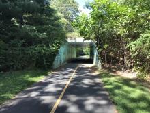A clear two lane roads leads to an overpass known as the Southwick Rail Trail Tunnel