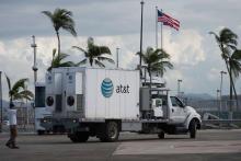 An AT&T truck is parked on a street with an American flag and palm trees in background